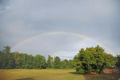 Full rainbow over the field forest and trees in summer after rain Stock Photos
