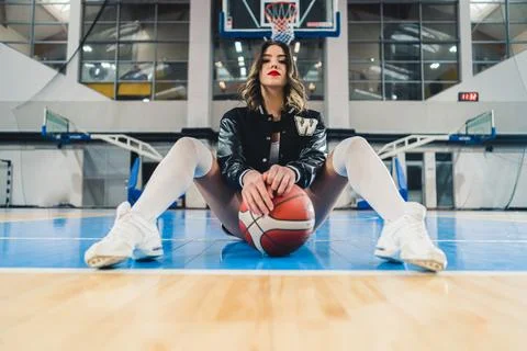 Full shot of a cheerleader posing with a ball on the arena floor, indoors Stock Photos