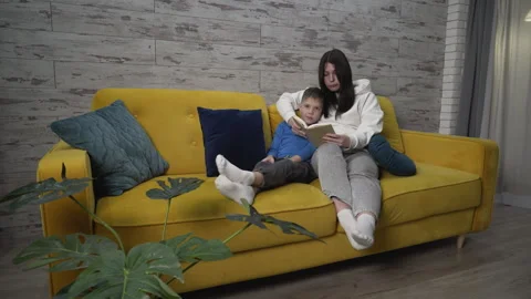 Full shot mom and son sitting on the couch reading a book Stock Footage 256981453
