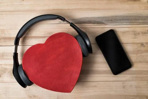 Full-size wireless headphones pulled over red heart-shaped box and smartphone Stock-Fotos