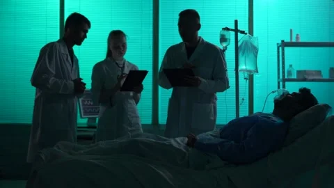 Full-sized silhouette video of three doctors standing around a patient on a Stock Footage 251895113
