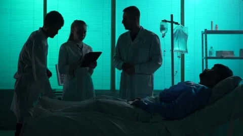 Full-sized silhouette video of three doctors standing around a patient laying in Stock Footage 251895355