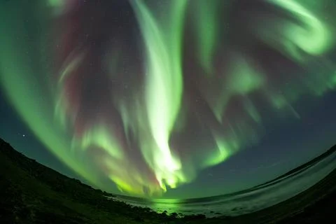 Full sky burning white aurora borealis over ocean Iceland Stock Photos