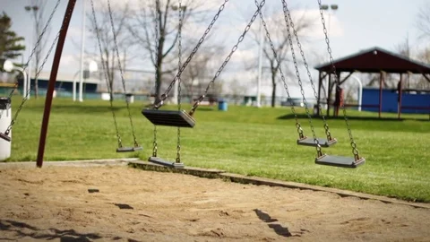 A full swingset swinging in the wind near school playground in park on sunny day Stock Footage
