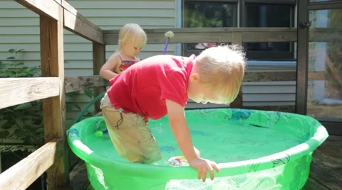Fully clothed boy swoops a toy through a kiddie pool Stock Footage 40028271