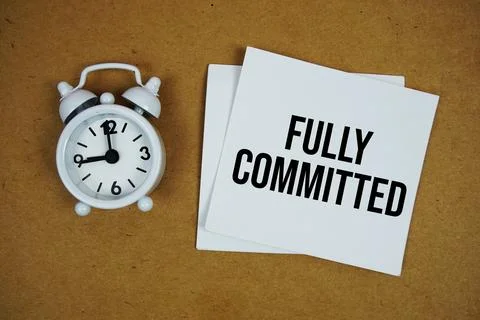 Fully Committed text on sticky note with alarm clock on paper craft backgroun Stock Photos