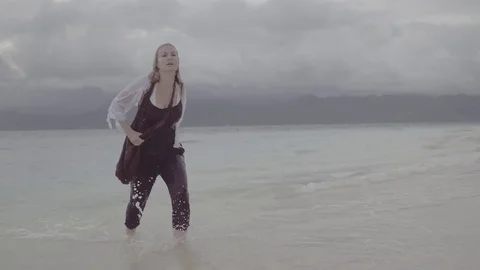 Fully dressed woman walks out of water towards camera Stock Footage