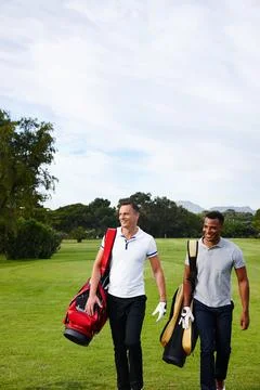 Fun and exercise. two men walking across a golf course with their golf bags. Fotos de archivo