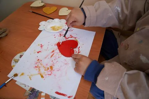 Fun art session. Boy paints heart with red paint for valentine's day. Stock Photos