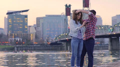 Fun Couple Stand On Dock To Take Selfies, Crew Boats Row Past In Background Stock Footage 61042572
