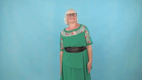 Fun expressive and energetic old woman dancing on a blue background Stock Footage 113865013