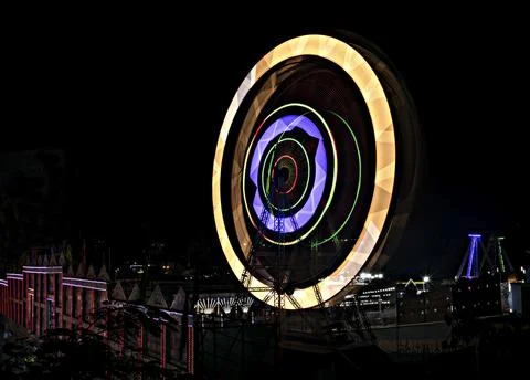 Fun fair Giant Colorful Ferris wheel spinning at night. Slow shutter image of Stock Photos