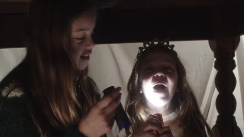 Fun flashlight games with girls under a table at night indoors Stock Footage 320030645