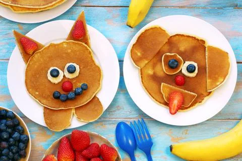 Fun food for kids. Cat and dog shaped pancakes with berries on blue wooden table Stock Photos