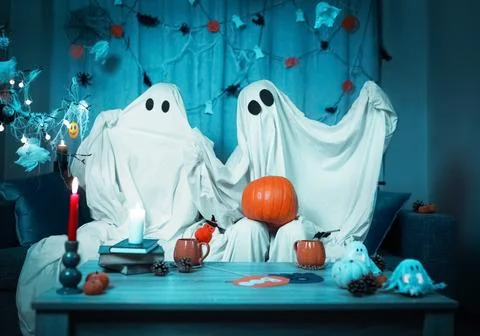 Fun Halloween couple dressed as ghosts hold a pumpkin at home. The room fea.. Stock Photos
