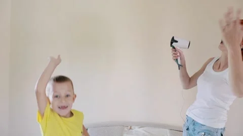 Fun Mom and son are jumping on the bed. Redhead girl singing while holding a hai Stock Footage 156300947