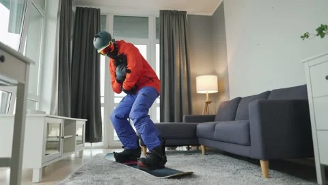 Fun video. Man dressed as a snowboarder rides a snowboard on a carpet in a cozy Stock Footage 144912972