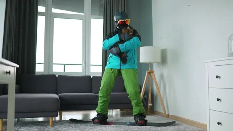 Fun video. Man dressed as a snowboarder rides a snowboard on a carpet in a cozy Stock Footage 153973632