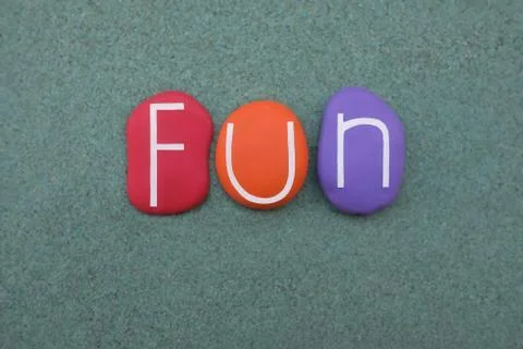 Fun word composed with multicolored stone letters over green sand Stock Photos