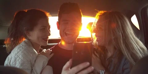 Fun Young Womens and man laugh and do a selfie In Back Seat Of Moving Car. Slow Stock Footage 154457397