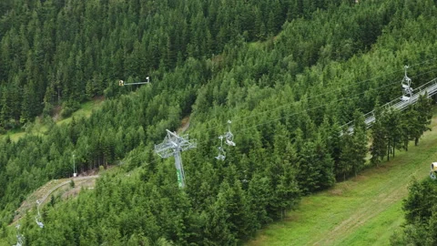 Functioning chairlift driving up hill slope among forests Video stock 204871085