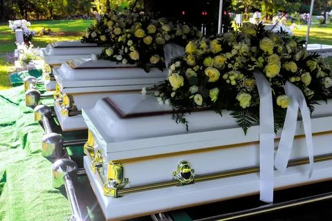 Funeral ceremony with multiple caskets covered in flowers at cemetery Stock Photos