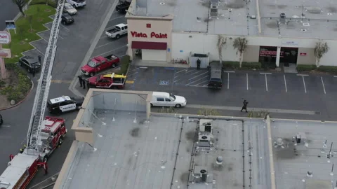 A funeral procession, lead by a white hearse approaches a building. Aerial Stock Footage 172550368