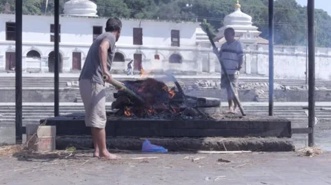Funeral pyre on a ghat with two men stoking the burning wood 動画素材 45987040