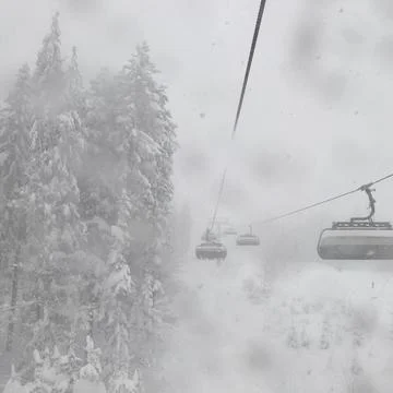 Funicular over forest in the mountains during a snow blizzard. I Stock Photos