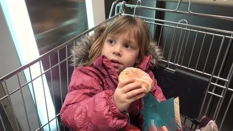 A funny 4-5 year old girl sits in a cart and eats a donut. Видео 83828213