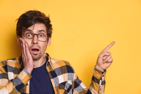 Funny amazed guy pointing at copy space on yellow studio background Stock Photos