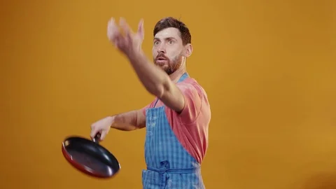 Funny attractive chef in apron playing with frying pan on background. Portrait Видео 125819282