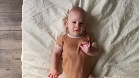 Funny baby boy lying on back near bed side looking at camera. Emotional adorable Stock Footage 245667646