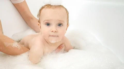 Funny baby boy with soap foam on head playing in bathroom with toy boats and Stock Photos