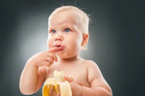 Funny baby making faces while holding banana Stock Photos