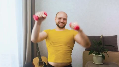 Funny bald man nerd dancing and doing aerobics with pink dumbbells at home Stock-Footage 243754626