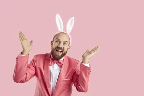 Funny bearded man in Easter bunny costume playing peekaboo on pink studio Stock Photos
