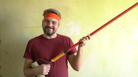 Funny bearded man holds a construction roller in his hands and plays like a Stock Footage 126124918