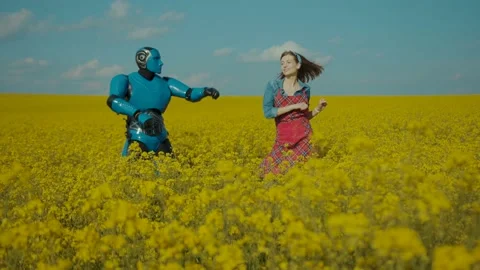 Funny blue robot and young happy woman farmer dancing on flower field with blue Stock Footage 133296563