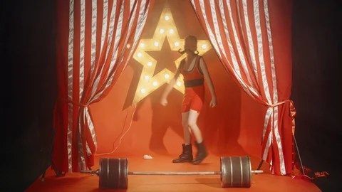 Funny boy circus strongman pushing up fake barbell Stock Footage 93585312