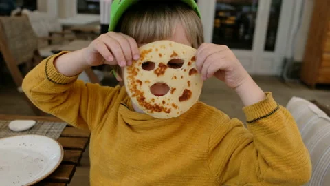 Funny boy fooling, making a mask from pancake in a restaurant Stock Footage 107371829
