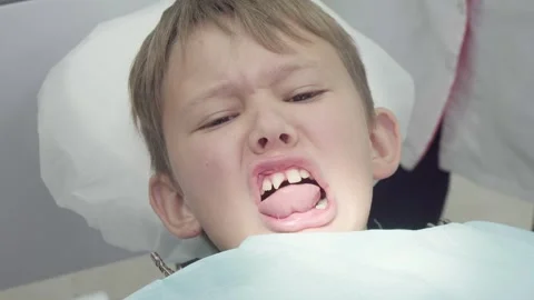 Funny boy makes faces in dental chair showing a chipped tooth Stock Footage 330482552