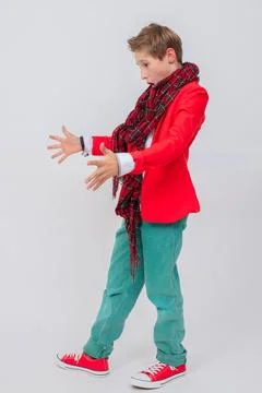 A funny boy in a red jacket, green jeans and sneakers in full growth on a g.. Stock Photos