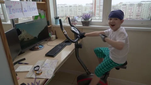Funny Boy Is Riding On Exercise Bike At Home. He Is Imagining Himself a Parti Video stock 129586909