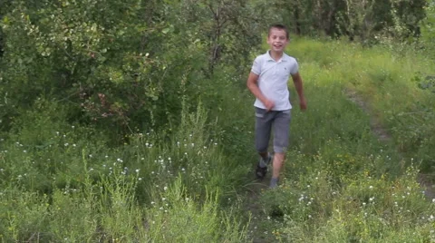 Funny boy running along the road surrounded by green trees and grass Vidéo 64921933