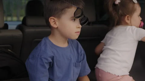 Funny boy sitting with his younger sister in the car, with sunglasses on his Stock Footage 258160835