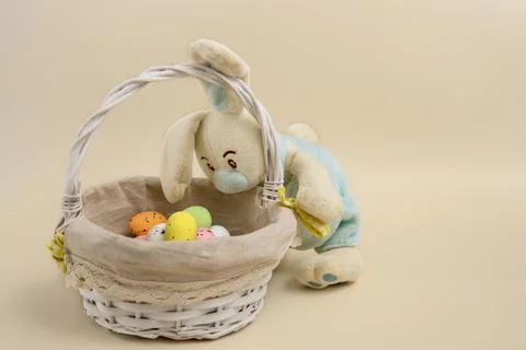 Funny bunny peeks into a basket with easter eggs on a beige background Stock Photos