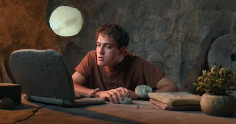 Funny Caveman Using Stone Mouse and Working on Laptop in Prehistoric Cave Stock Footage 337217425