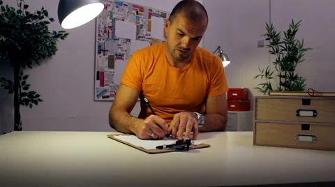 Funny character working late at the office under a desk lamp, puts away his work Vídeo Stock 32723780