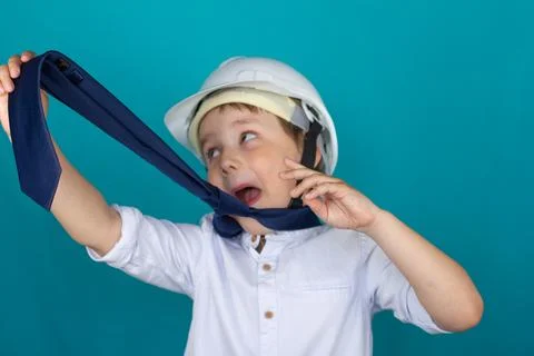 A funny child in a construction helmet pulls his tie and rolls his eyes. The Stock Photos